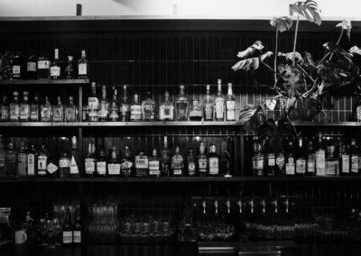 A black and white image showcasing liquor bottles on bar shelves with plants.