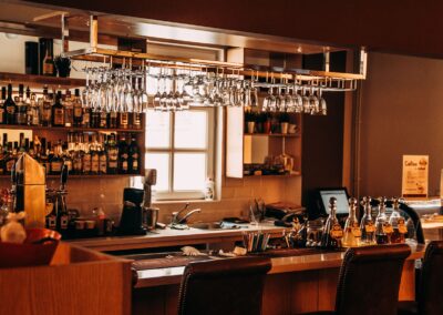 A stylish bar interior featuring hanging glassware, a range of spirits, and wooden furnishings.